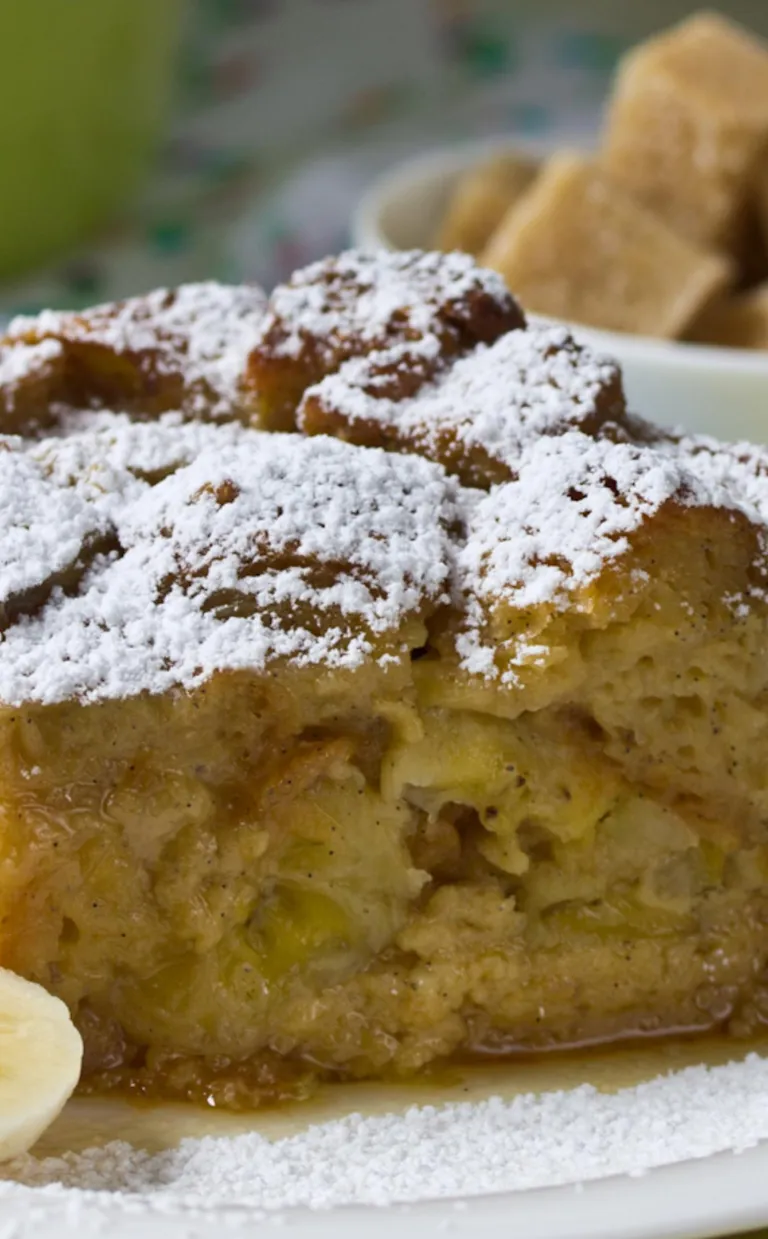 Banana Bread Pudding Recipe a square of banana bread pudding sprinkled with powdered sugar and sliced bananas on the side